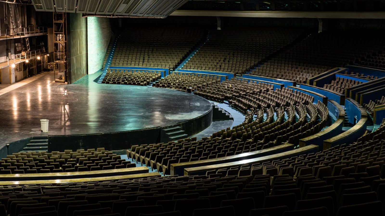 A large, empty auditorium with a circular stage and retro seating design.
