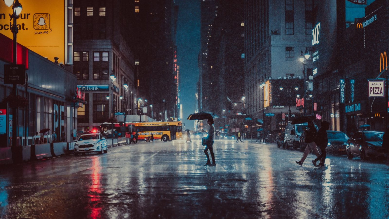 A rainy evening in New York City with people crossing a wet street under umbrellas.