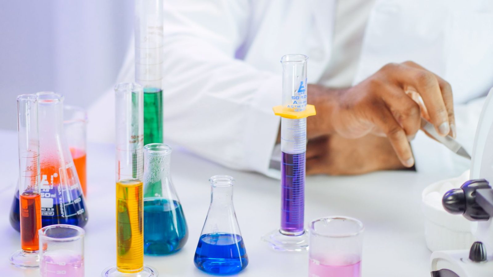 A scientist's hand working with colorful liquids in a laboratory setting.