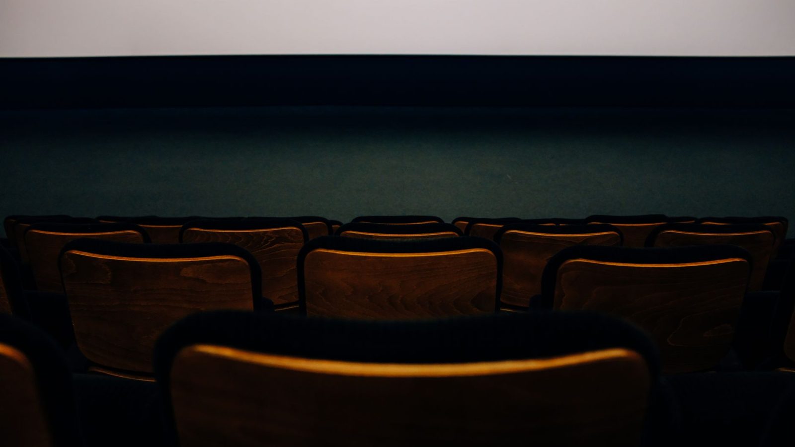 An empty auditorium with wooden seats facing a blank theater screen.
