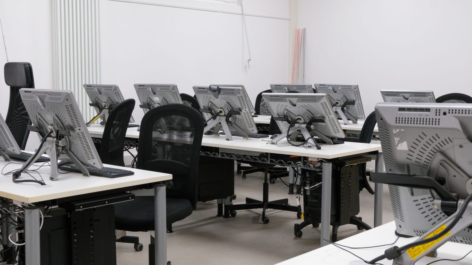 An empty computer lab featuring multiple workstations with monitors and chairs, ready for use.