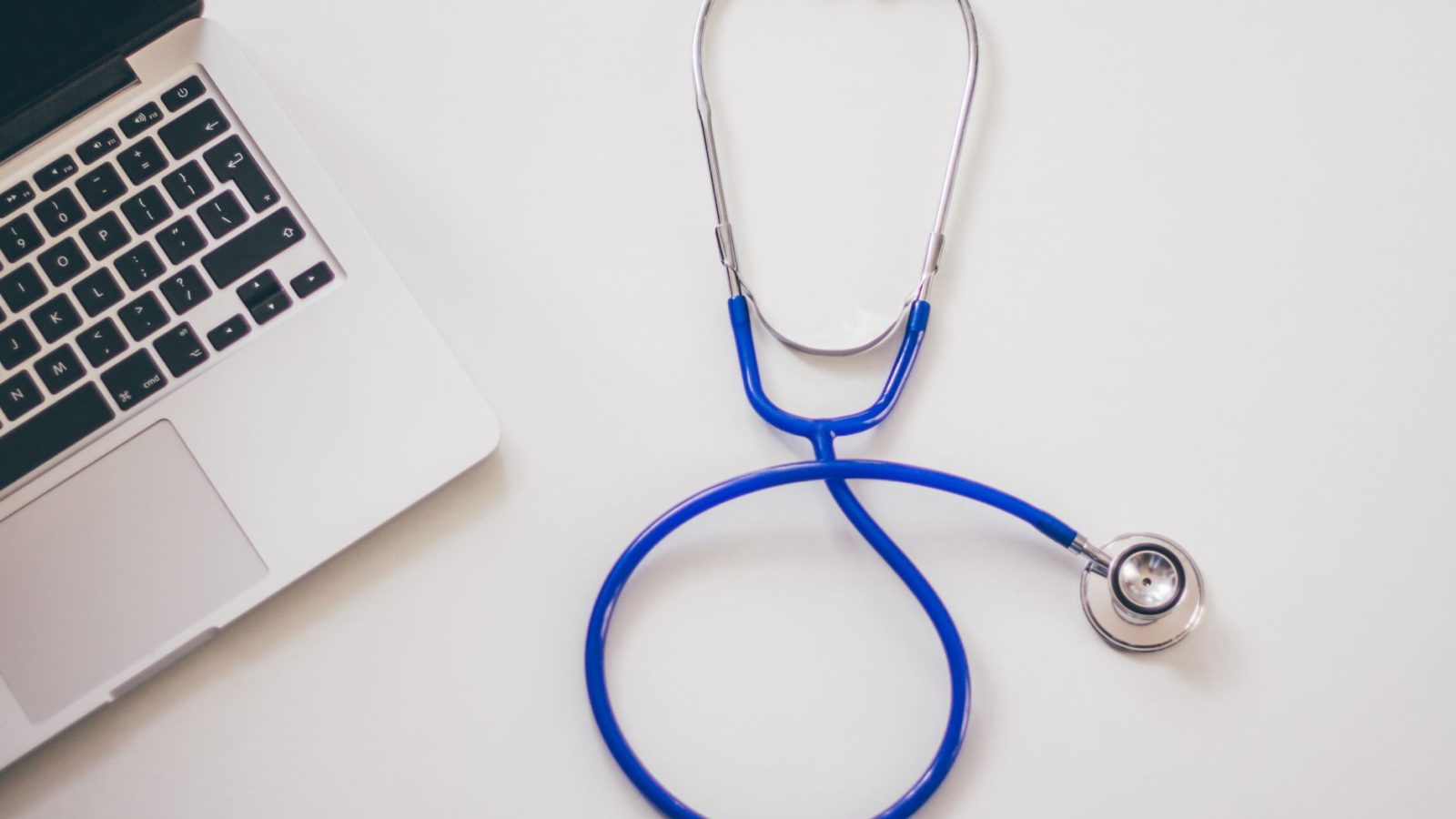 Medical stethoscope and laptop on a white desk, symbolizing digital health solutions.
