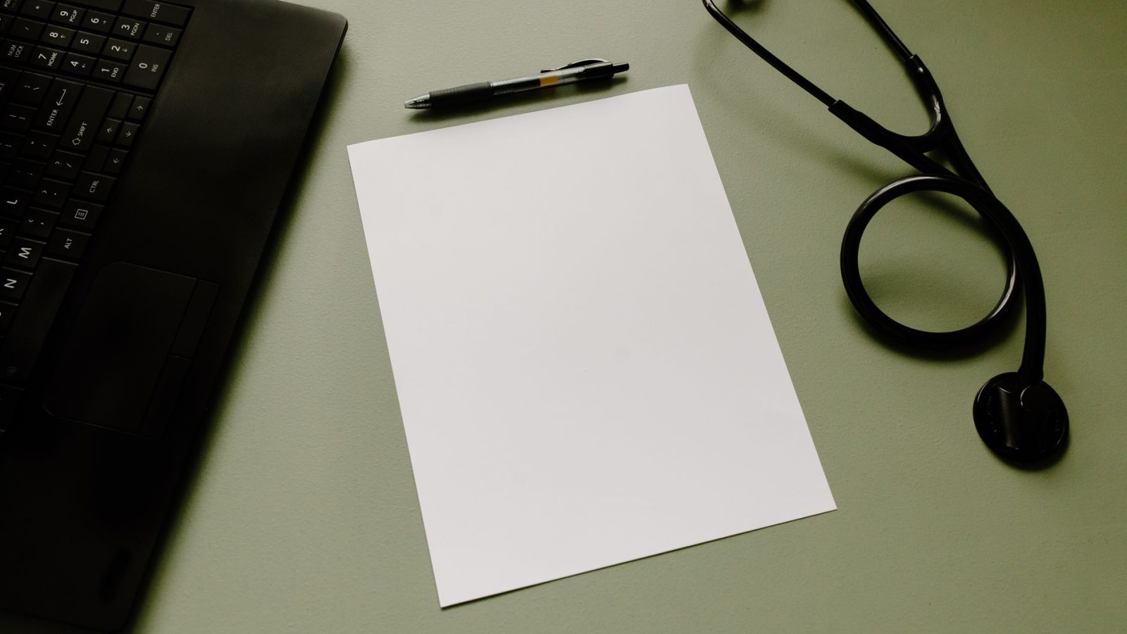 Professional workspace featuring a laptop, stethoscope, pen, and paper sheet for healthcare tasks.
