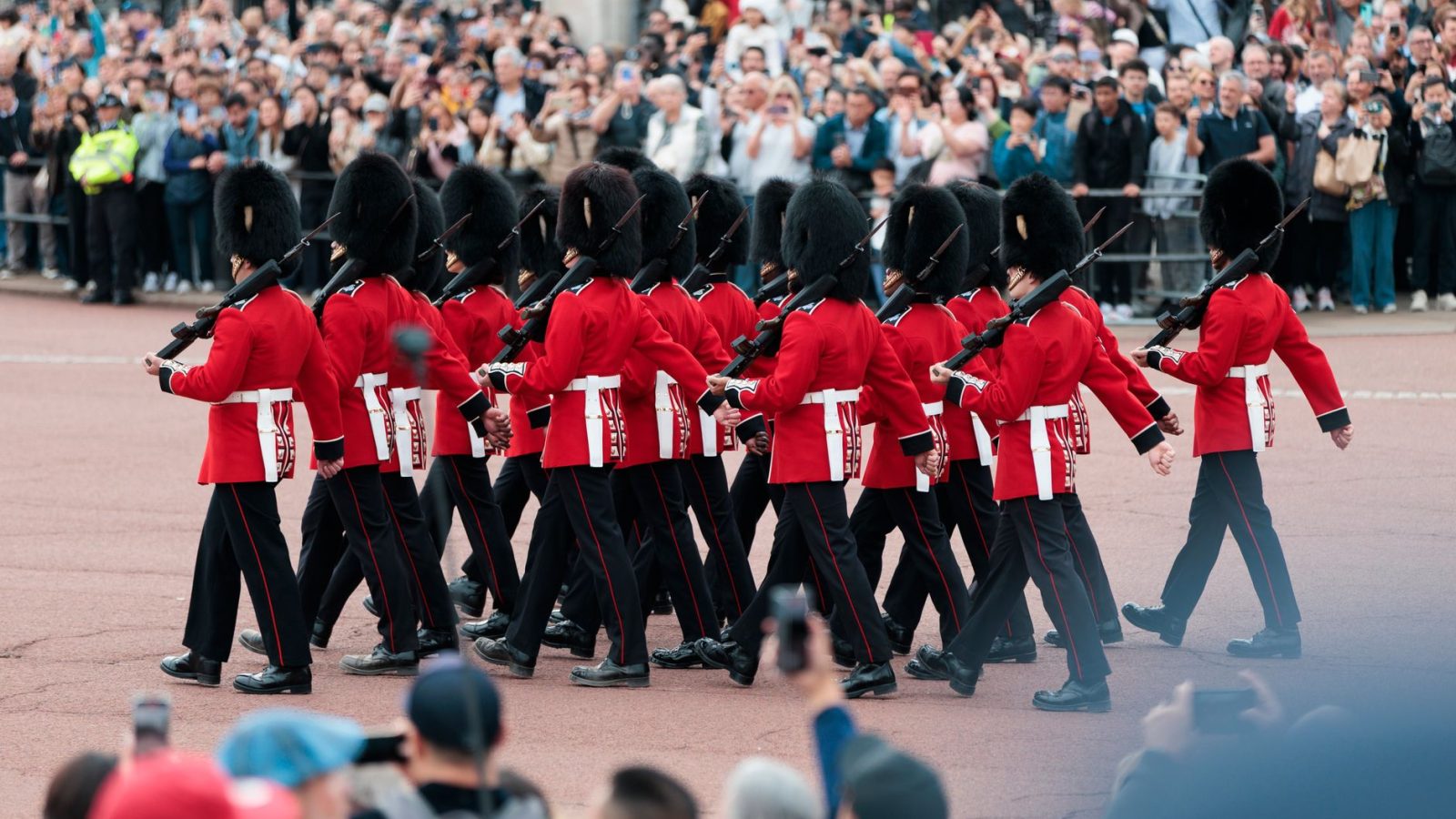 Changing of the Guard ceremony at Buckingham Palace, London, featuring soldiers in traditional red uniforms.