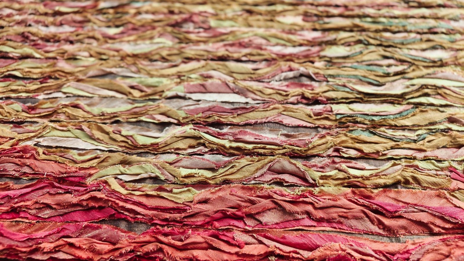 Colorful abstract textile art featuring layered and textured fabric swatches in warm tones.